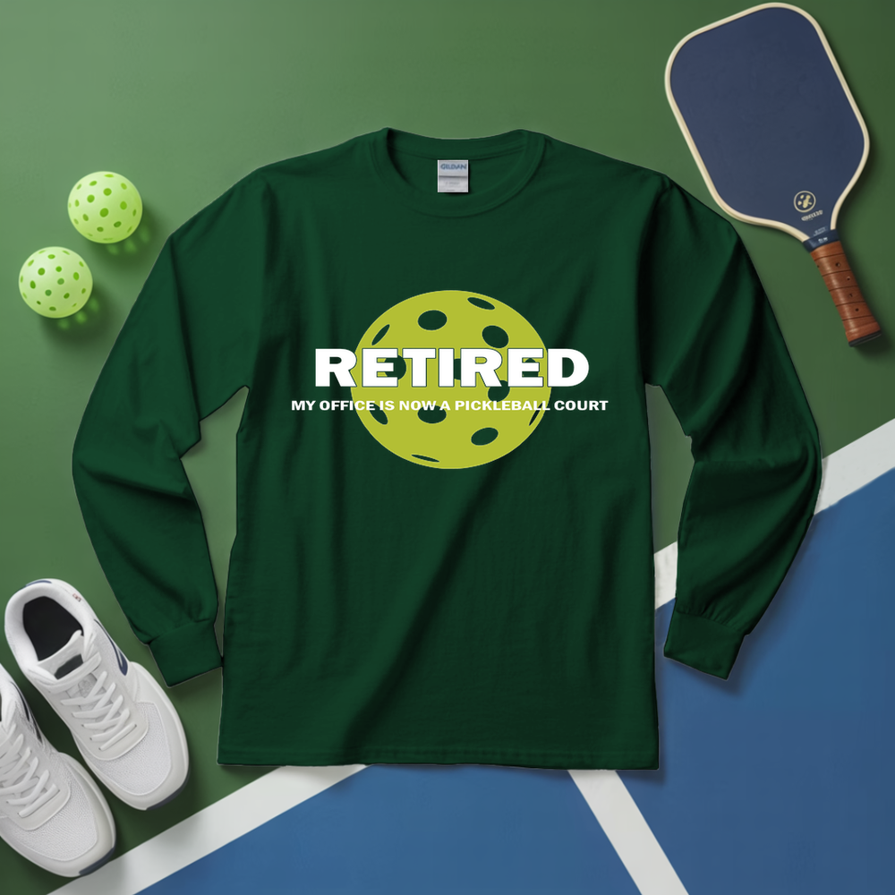 Green long-sleeve shirt with pickleball design and text on a green and blue surface with pickleballs and a paddle.