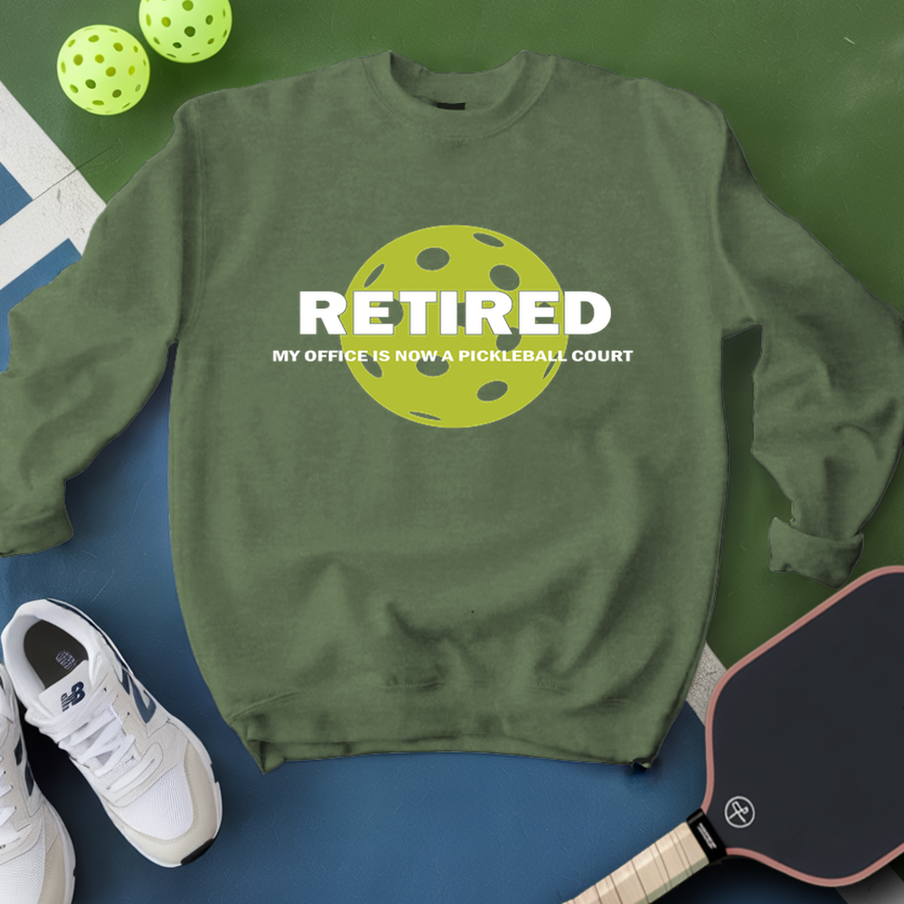 Green sweatshirt with pickleball design and text, surrounded by pickleballs and a paddle on a green and blue background.