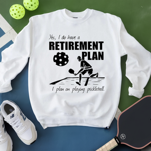 White sweatshirt with pickleball-themed design on a green and blue surface with pickleballs and a paddle.