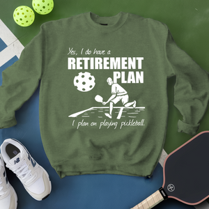 Green sweatshirt with pickleball-themed design and text, surrounded by pickleballs and a paddle on a green and blue background.
