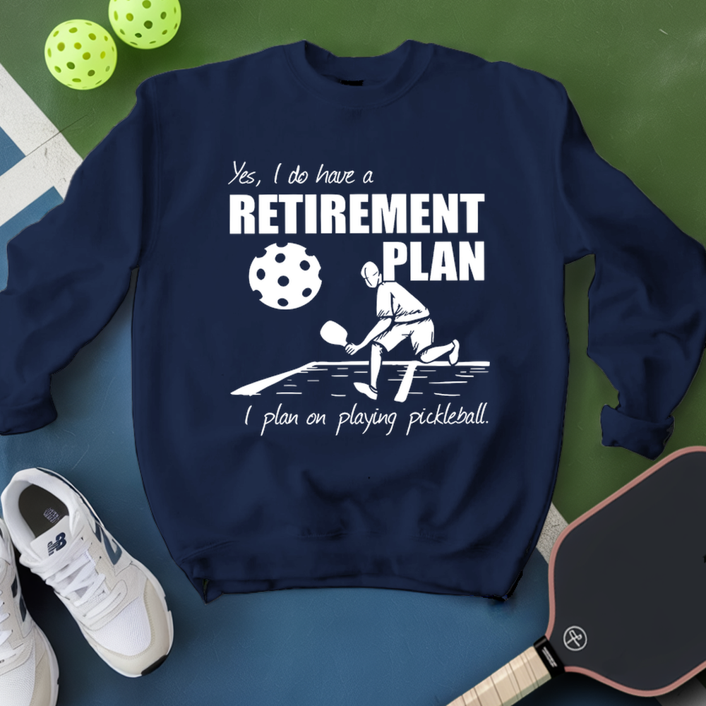 Navy blue sweatshirt with pickleball-themed design and text, placed on a green and blue surface with pickleballs and a paddle.