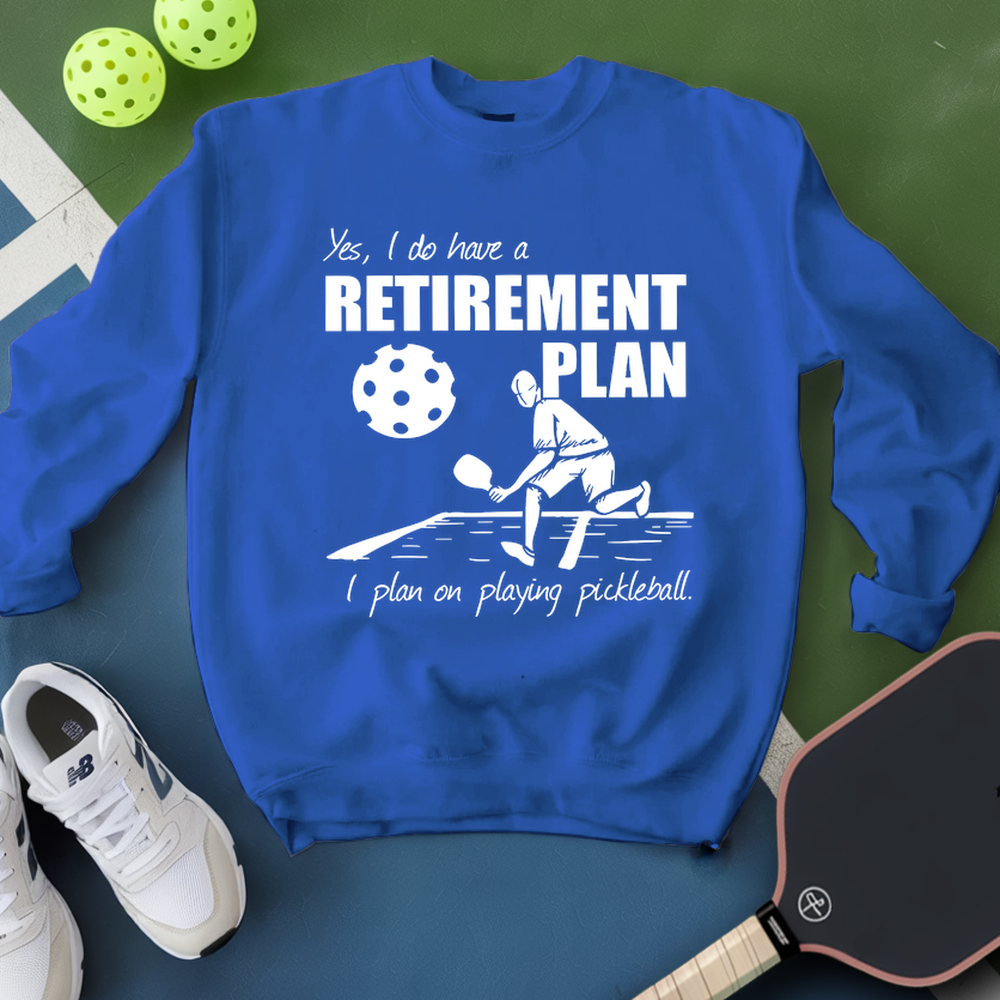 Blue sweatshirt with pickleball-themed design on a green surface with pickleballs and shoes.