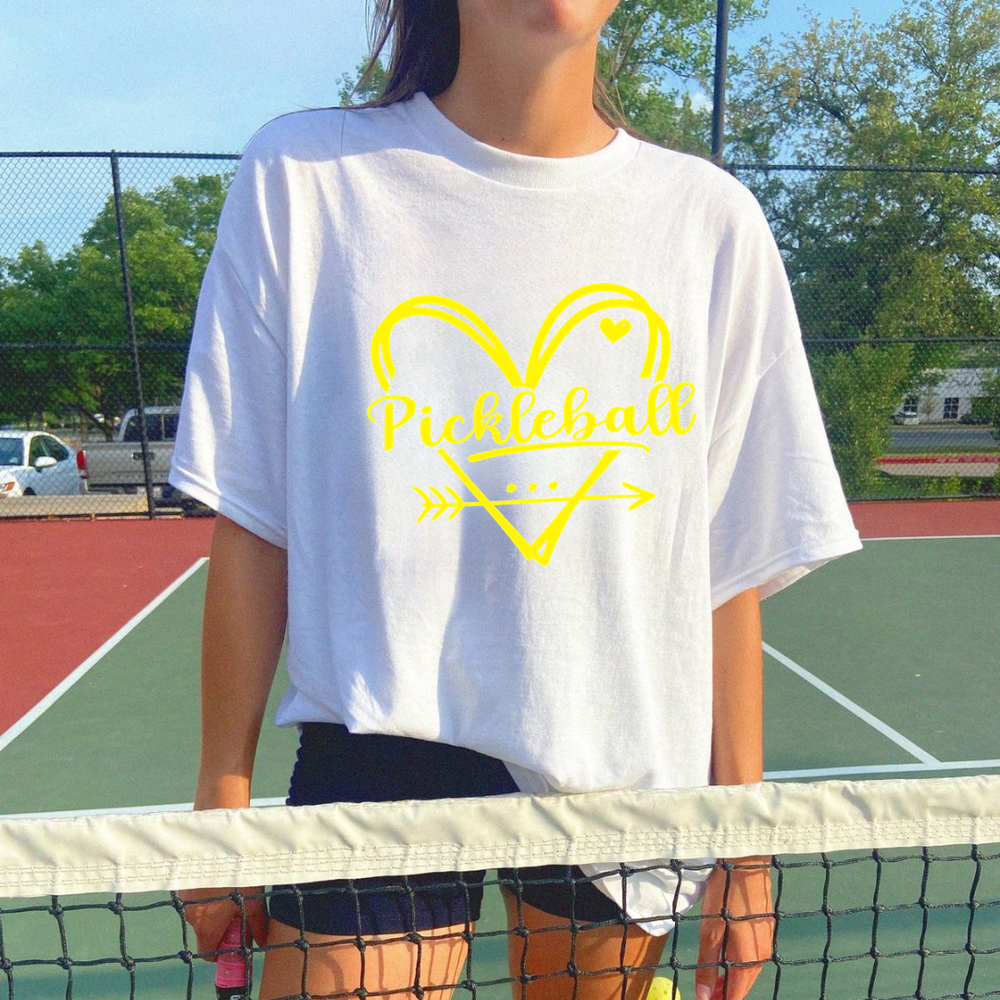 Person wearing a white t-shirt with yellow 'Pickleball' design on a tennis court