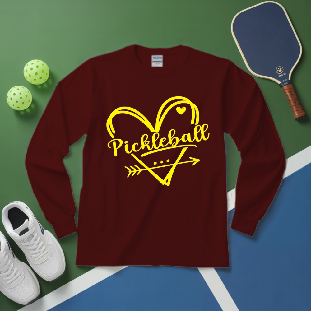 Navy long-sleeve shirt with yellow 'Pickleball' design on a green and blue surface with pickleball equipment.
