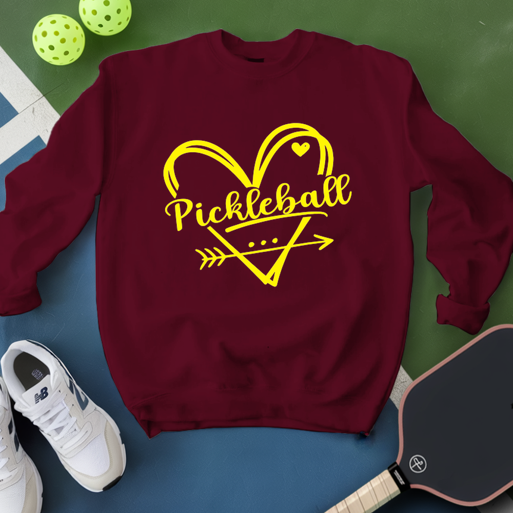 Navy sweatshirt with yellow 'Pickleball' design on a green and blue surface with pickleballs and a paddle.