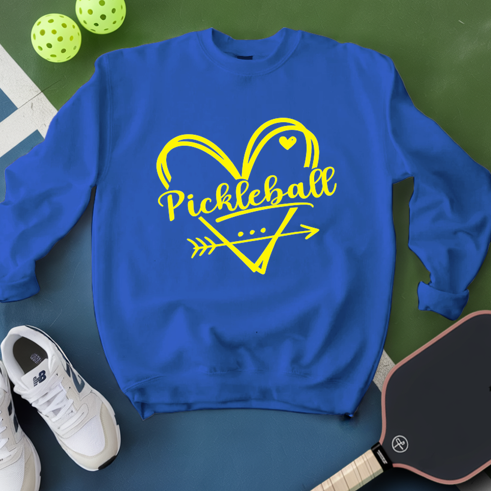 Blue sweatshirt with yellow 'Pickleball' design on a green surface with pickleballs and a paddle.