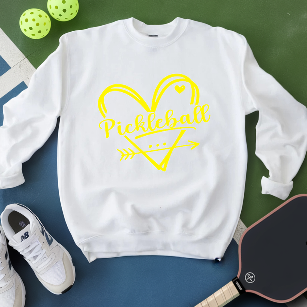 White sweatshirt with yellow 'Pickleball' design on a green and blue surface with pickleballs and a paddle.