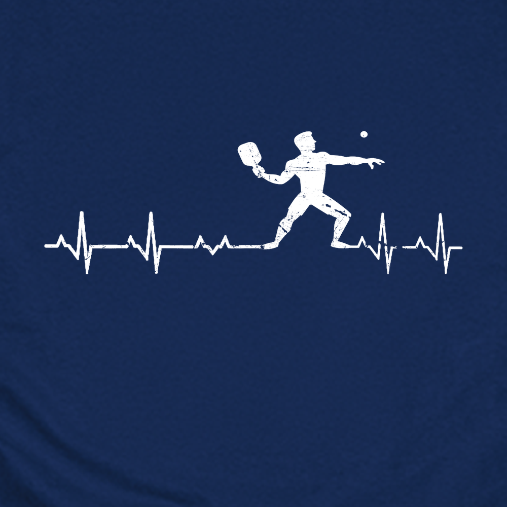 Navy blue t-shirt with pickleball player design and heart rate line, next to a paddle and ball on a white background