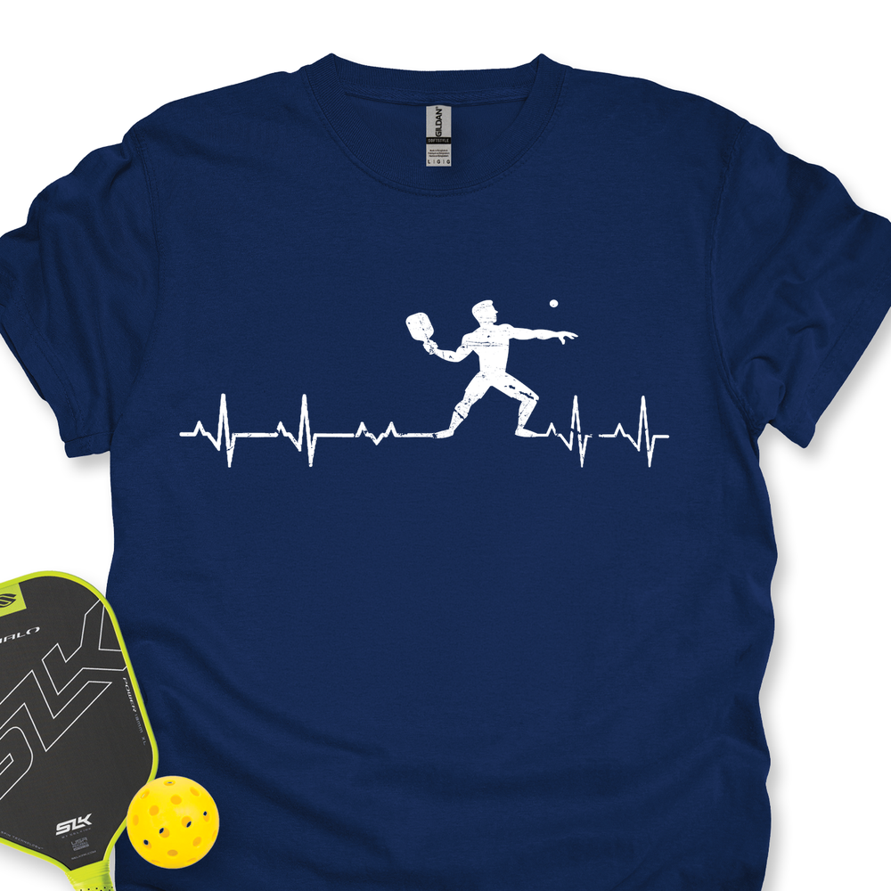 Navy blue t-shirt with pickleball player design and heart rate line, next to a paddle and ball on a white background