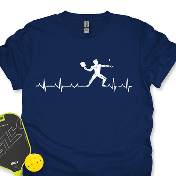 Navy blue t-shirt with pickleball player design and heart rate line, next to a paddle and ball on a white background