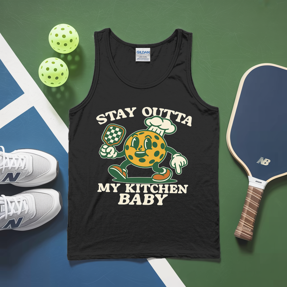 Black tank top with cartoon pickle design and text, placed on a green and blue surface with pickleball equipment.