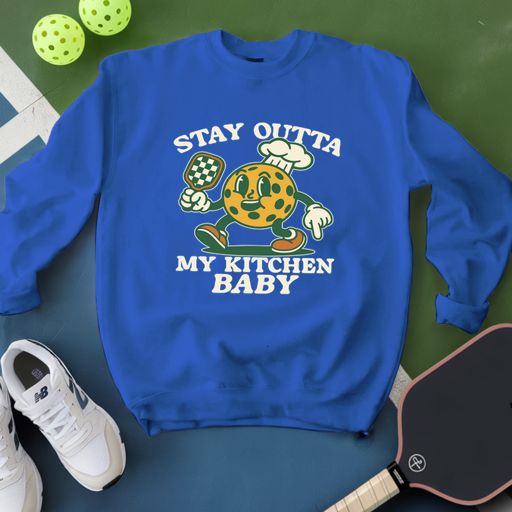 Blue sweatshirt with a cartoon character and text on a green surface with pickleball equipment.