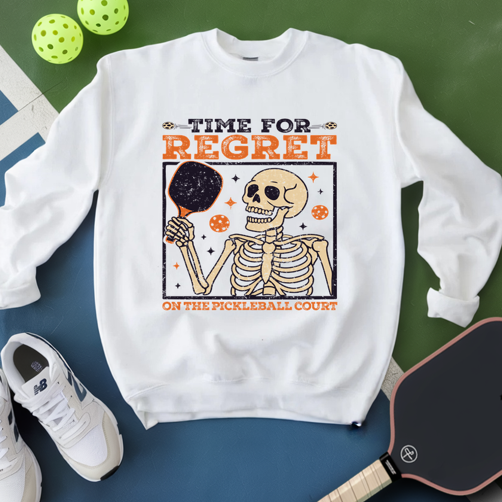 White sweatshirt with skeleton graphic and text on a green and blue background with pickleball equipment.