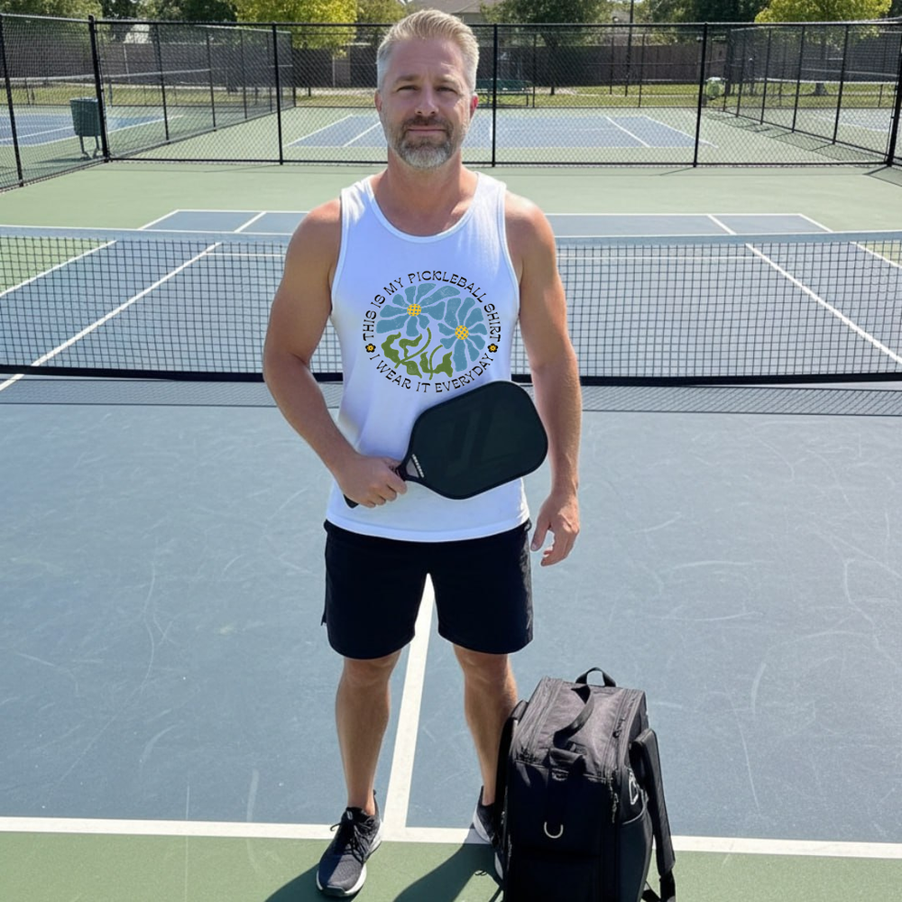 Man standing on a pickleball court holding a paddle and wearing a tank top with a pickleball design.