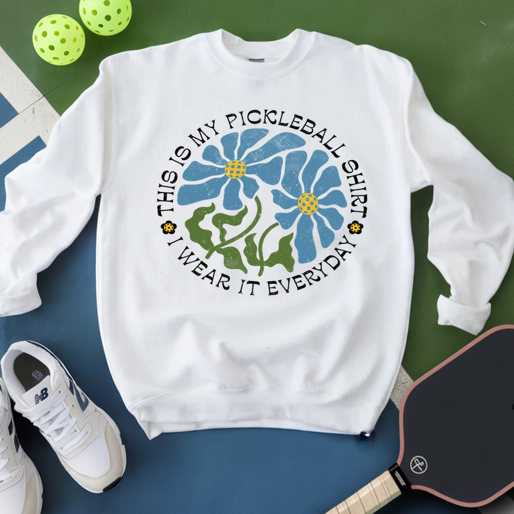 White sweatshirt with pickleball-themed design on a green and blue background
