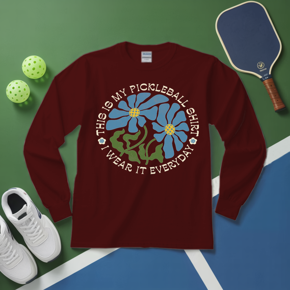 Maroon long-sleeve shirt with pickleball-themed design on a green and blue surface with pickleball equipment.