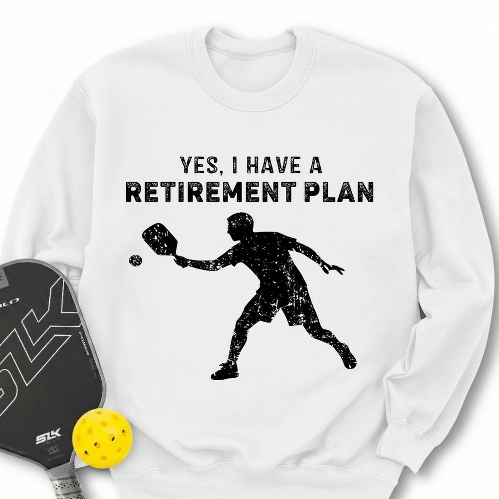 White sweatshirt with pickleball design and text, accompanied by a paddle and ball on a white background.