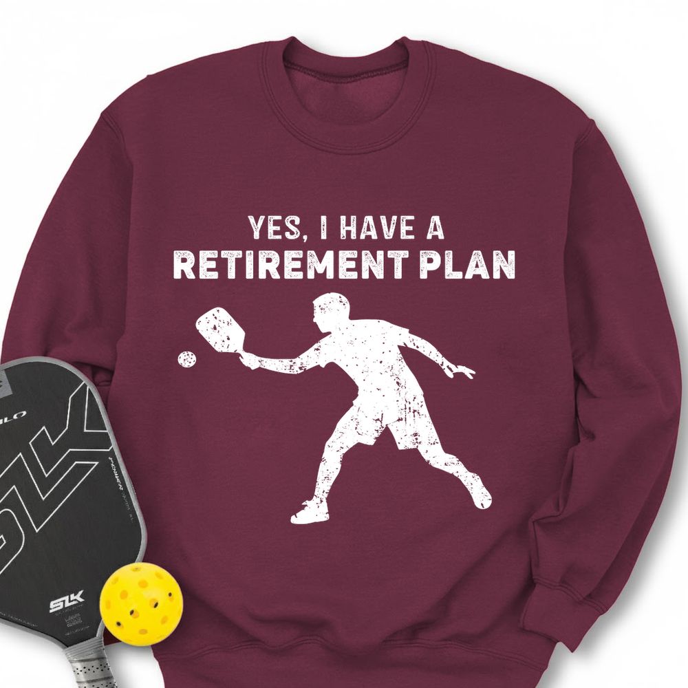Maroon sweatshirt with pickleball design and text, accompanied by a paddle and ball on a white background.