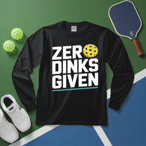 Black long-sleeve shirt with 'ZERO DINKS GIVEN' text on a sports court background with pickleball equipment.