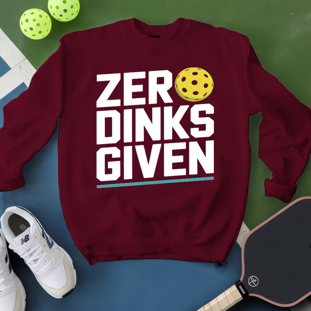 Maroon sweatshirt with 'ZER DINKS GIVEN' text and pickleball ball, next to white sneakers and paddle on green and blue background.
