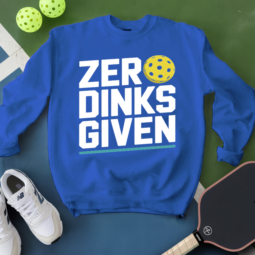 Blue sweatshirt with 'ZER DINKS GIVEN' text and pickleball ball on a green surface with shoes and paddle.