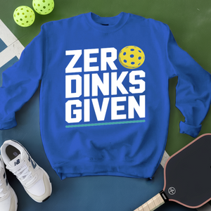 Blue sweatshirt with 'ZER DINKS GIVEN' text and pickleball ball on a green surface with shoes and paddle.