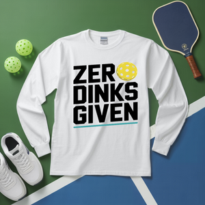 White long-sleeve shirt with 'ZER DINKS GIVEN' text, pickleball paddle, balls, and shoes on a green and blue surface.