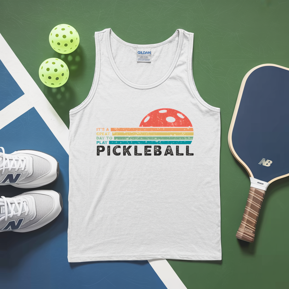 White tank top with pickleball design, pickleballs, and paddle on a green and blue surface