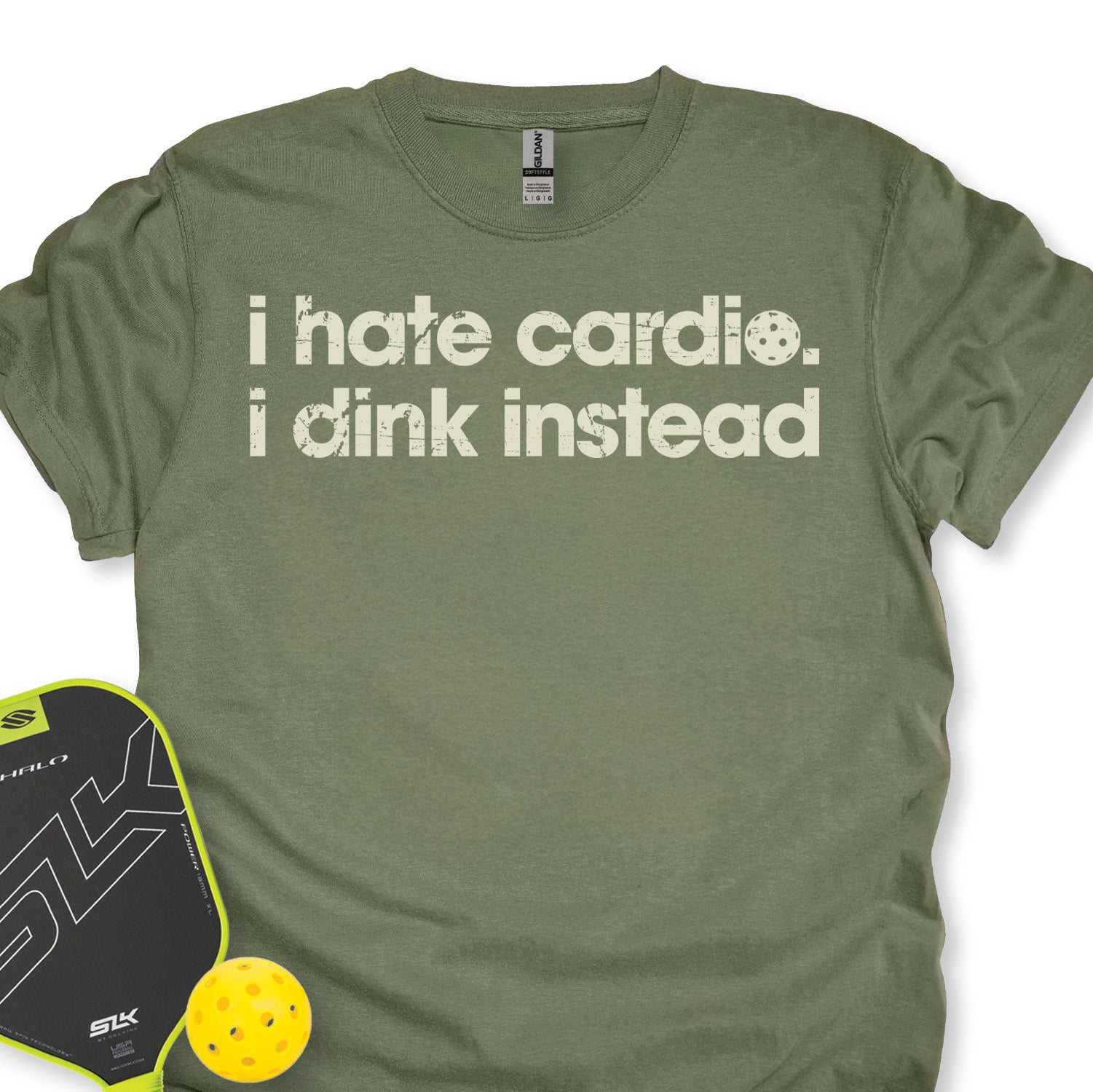 Green t-shirt with 'i hate cardio. i dink instead' text, next to a pickleball paddle and ball on a white background