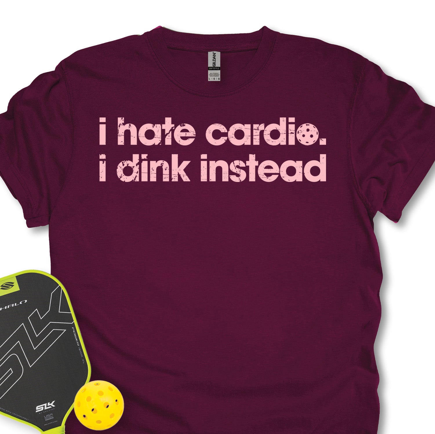 Maroon t-shirt with 'i hate cardio. i dink instead' text, next to a pickleball paddle and ball on a white background