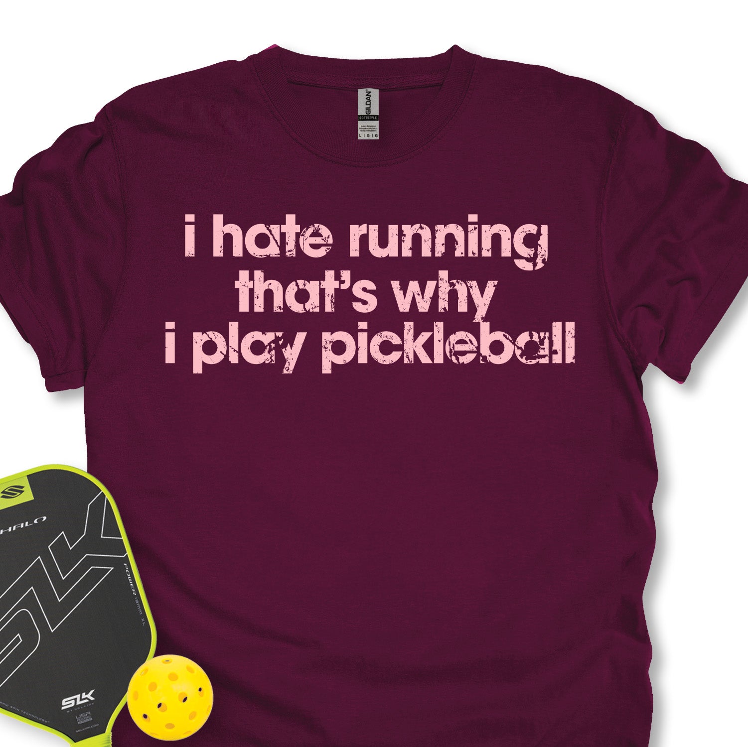 Maroon t-shirt with humorous pickleball text, next to a paddle and ball on a white background