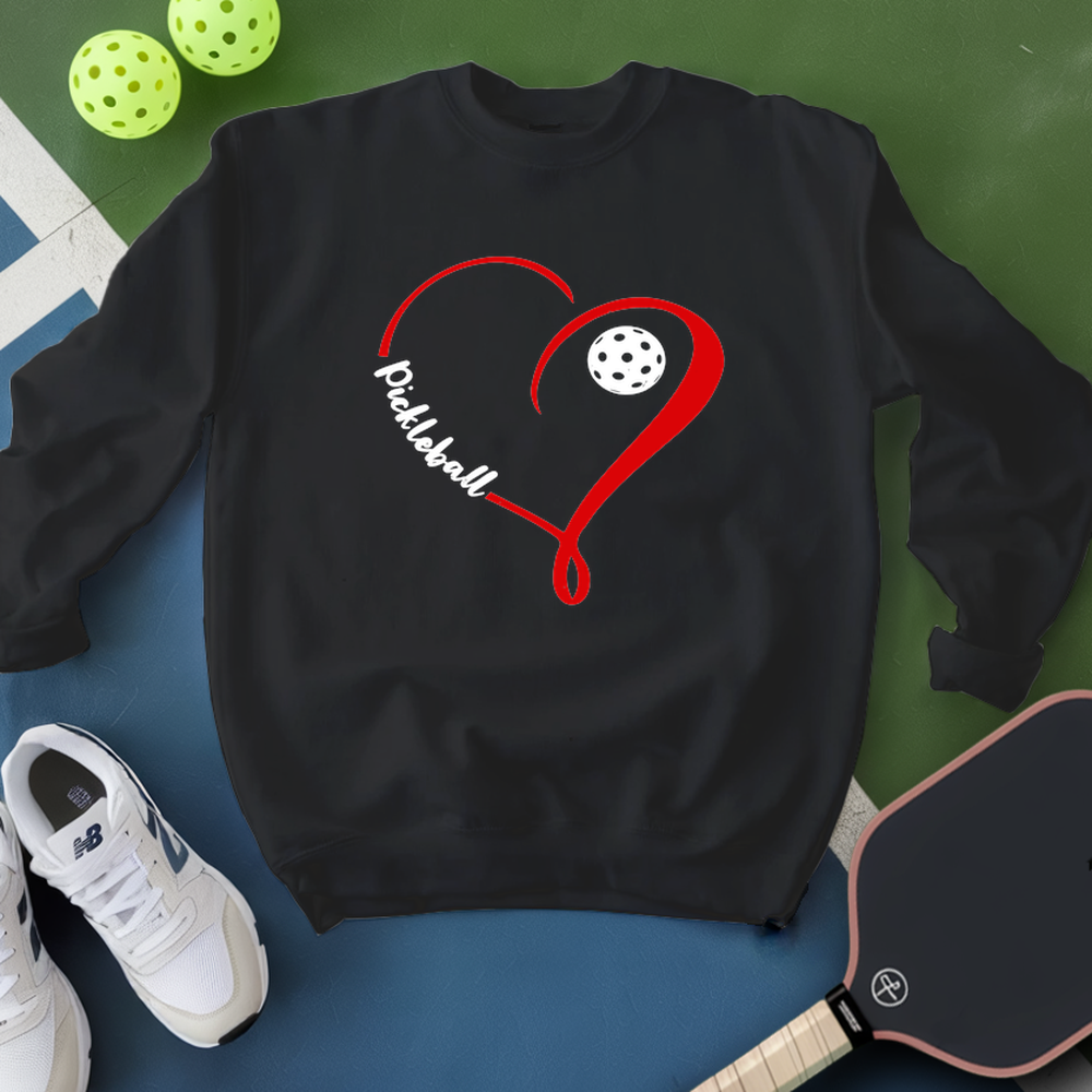 Black sweatshirt with red heart and pickleball design, surrounded by pickleballs and a paddle on a green and blue background.
