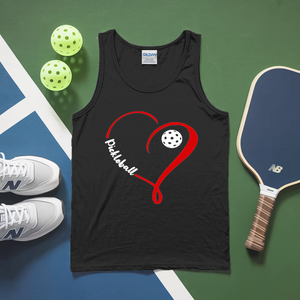 Black tank top with red heart and pickleball design, next to a paddle and balls on a green and blue surface.