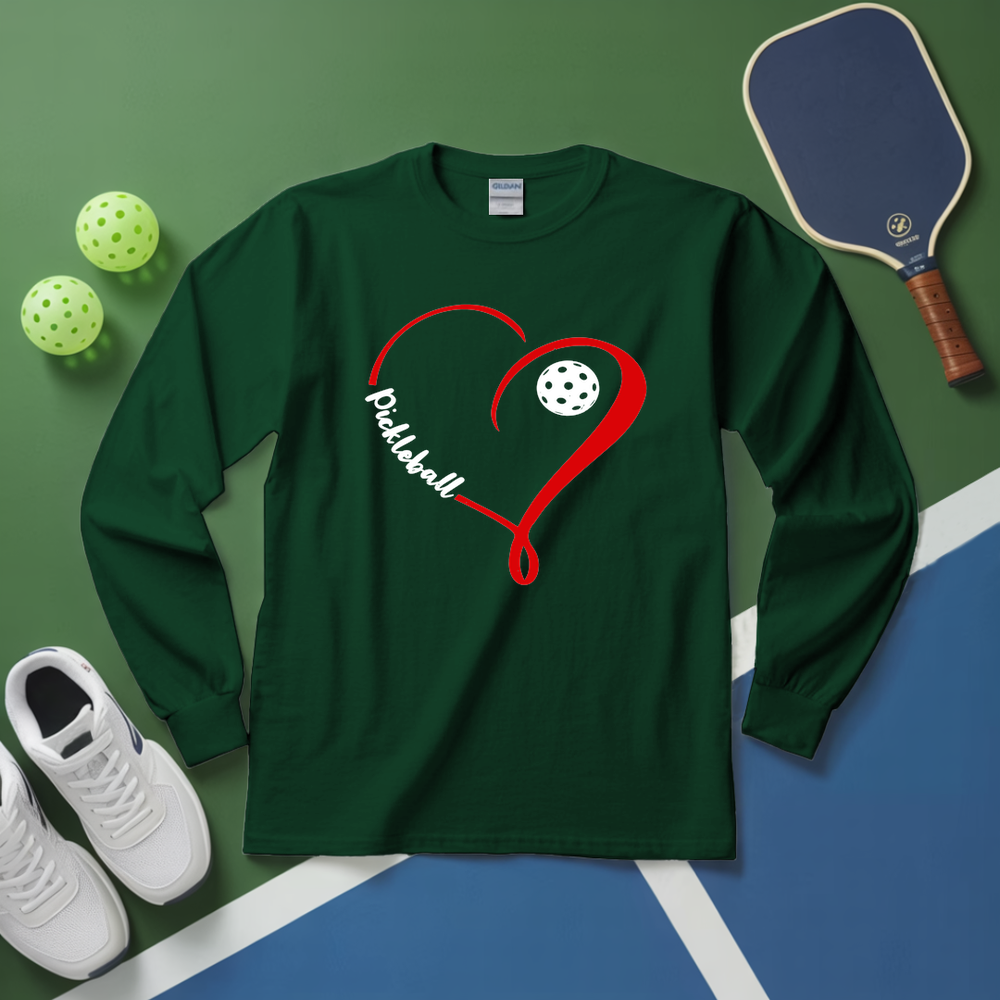 Green long-sleeve shirt with red heart design and pickleball text, placed on a green and blue surface with pickleball equipment.