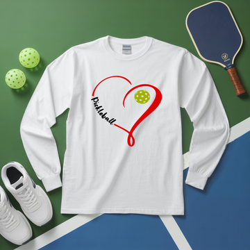 White long-sleeve shirt with pickleball design on a green and blue surface with pickleballs and a paddle.