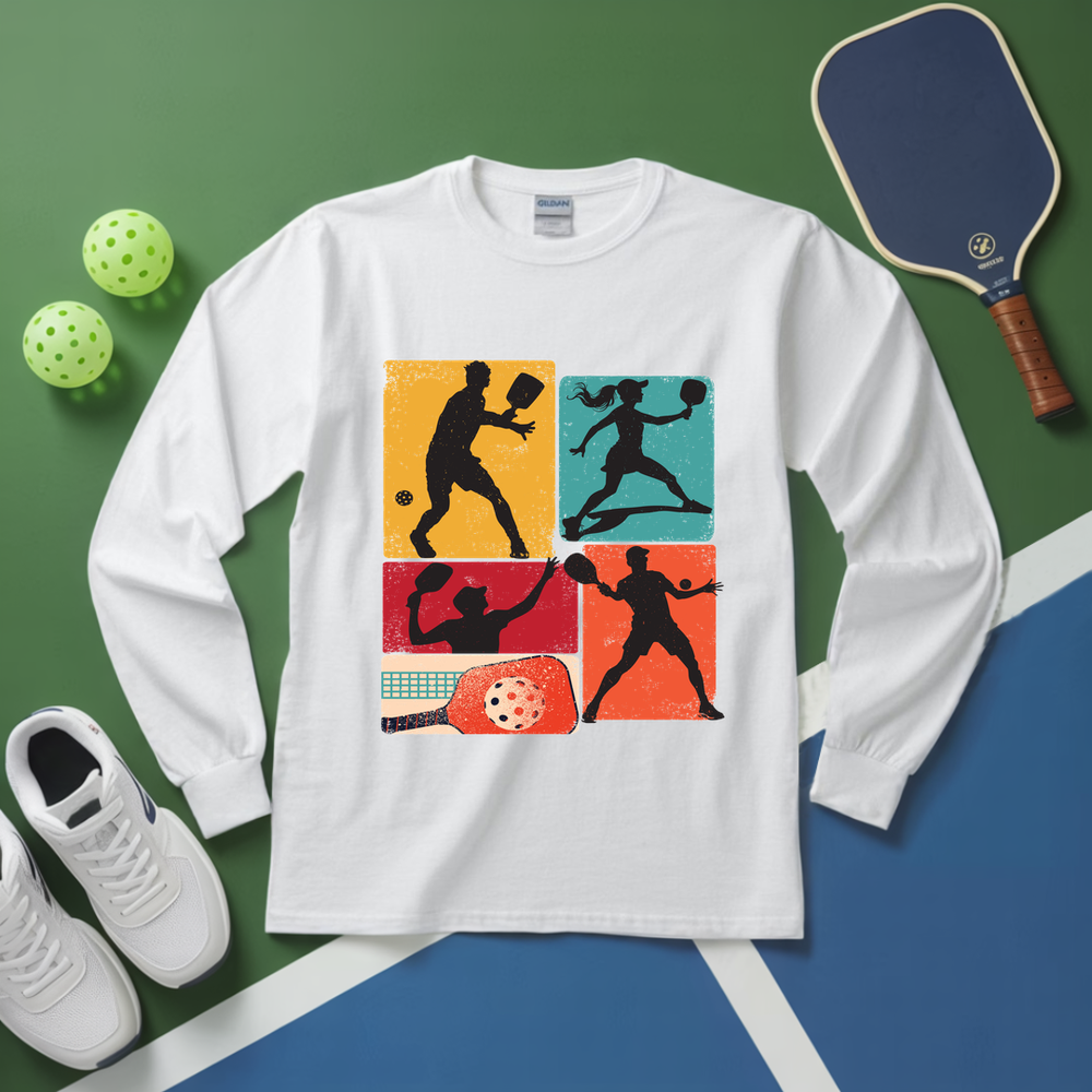 White long-sleeve shirt with pickleball-themed design on a green and blue surface with pickleball equipment.