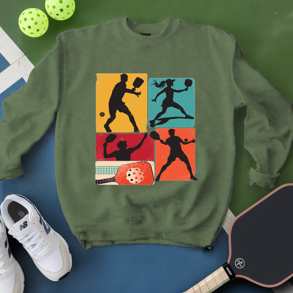Green sweatshirt with pickleball-themed design on a blue surface with pickleballs and paddle.