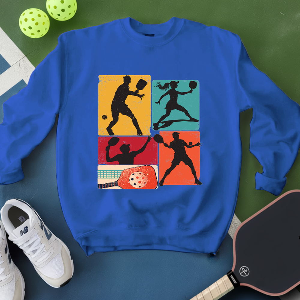 Blue sweatshirt with pickleball-themed design on a green and blue surface with pickleballs and a paddle.