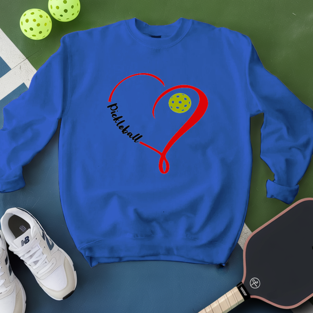 Blue sweatshirt with pickleball design on a green surface with pickleballs and a paddle.