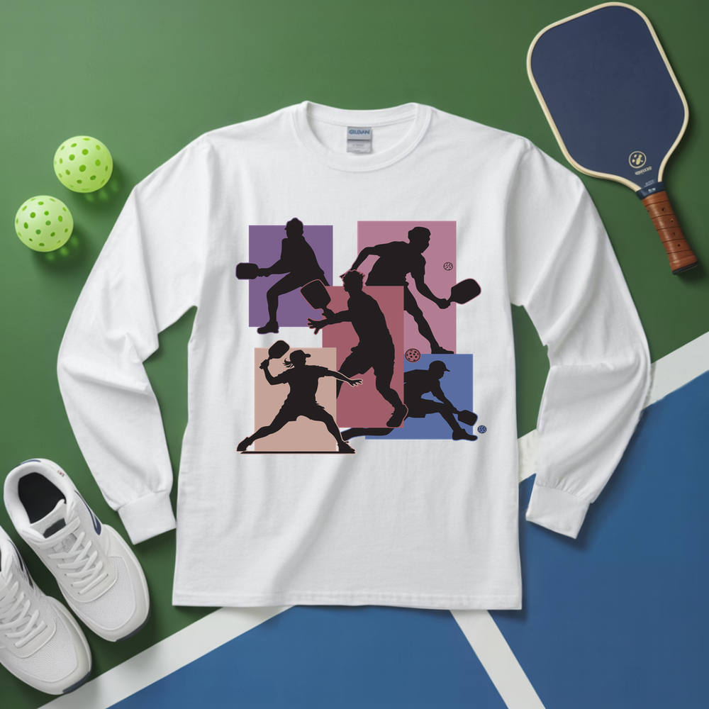 White long-sleeve shirt with pickleball player design on a green and blue surface with pickleball equipment.