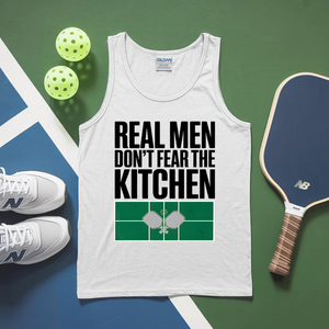 White tank top with 'Real Men Don't Fear The Kitchen' text, pickleball paddles, balls, and shoes on a green and blue background.