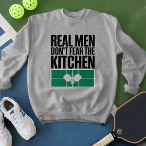 Gray sweatshirt with 'Real Men Don't Fear The Kitchen' text and pickleball equipment on a green and blue background